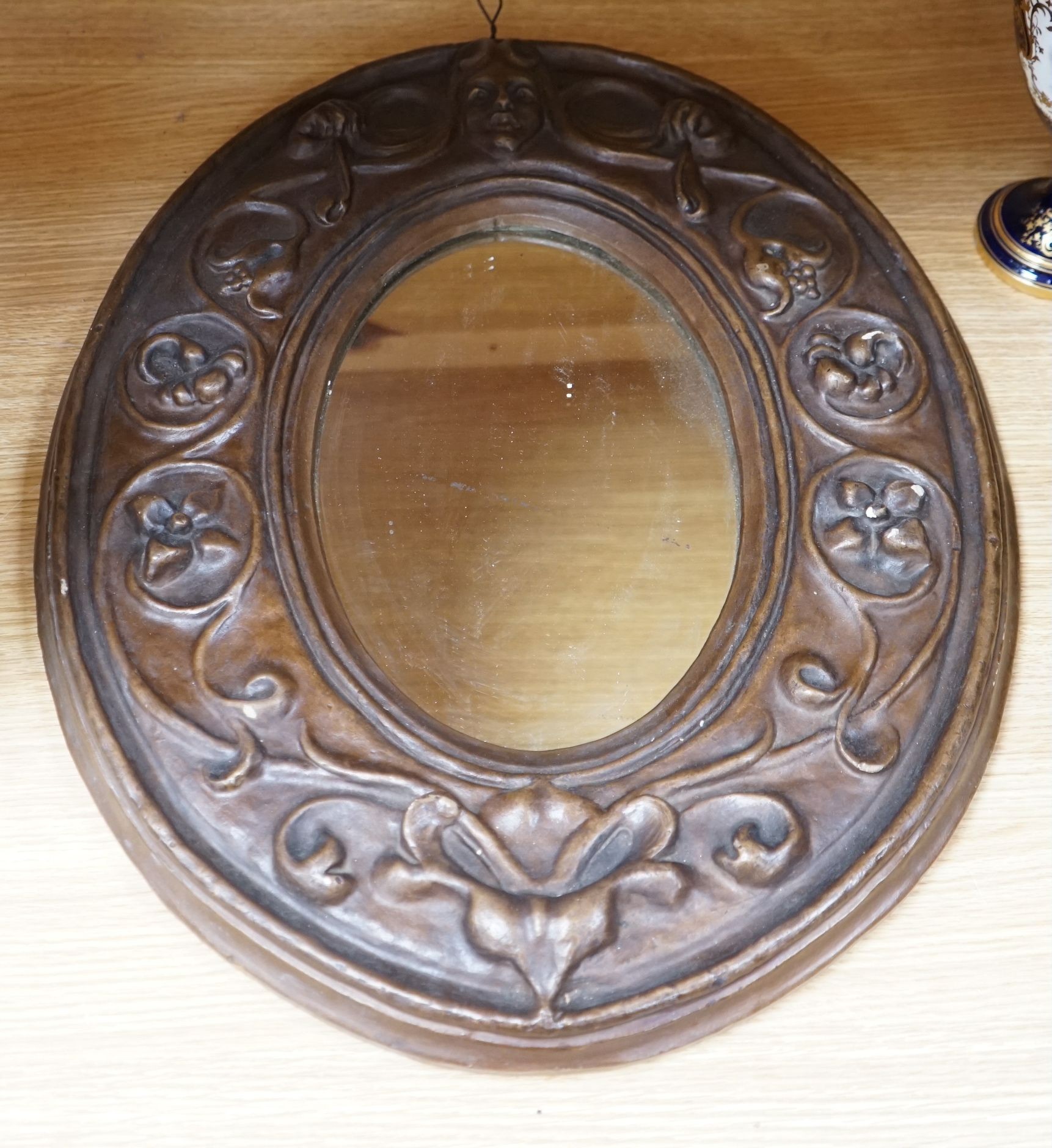 An Art Nouveau style moulded gesso oval mirror, 57cms high